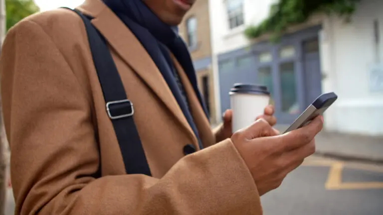 Close Up Of Man With Takeaway Coffee Checking Messages Or Social Media On Street Using Mobile Phone