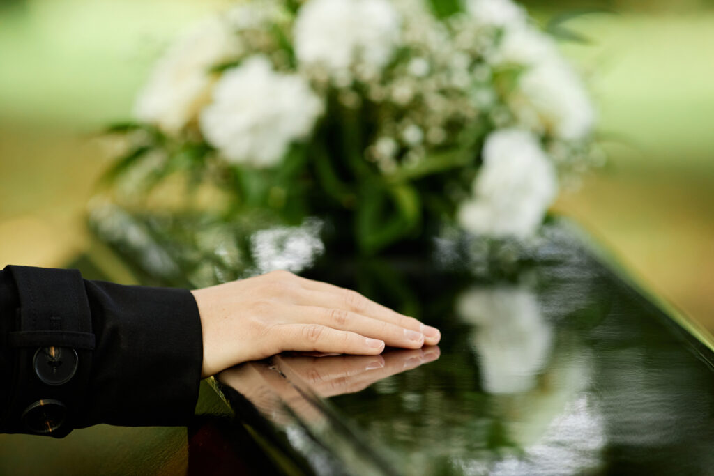 Hand on a coffin to represent funeral costs.