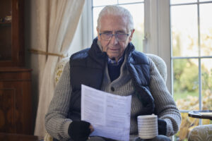 Older man wearing extra clothes with hot drink reading energy bill